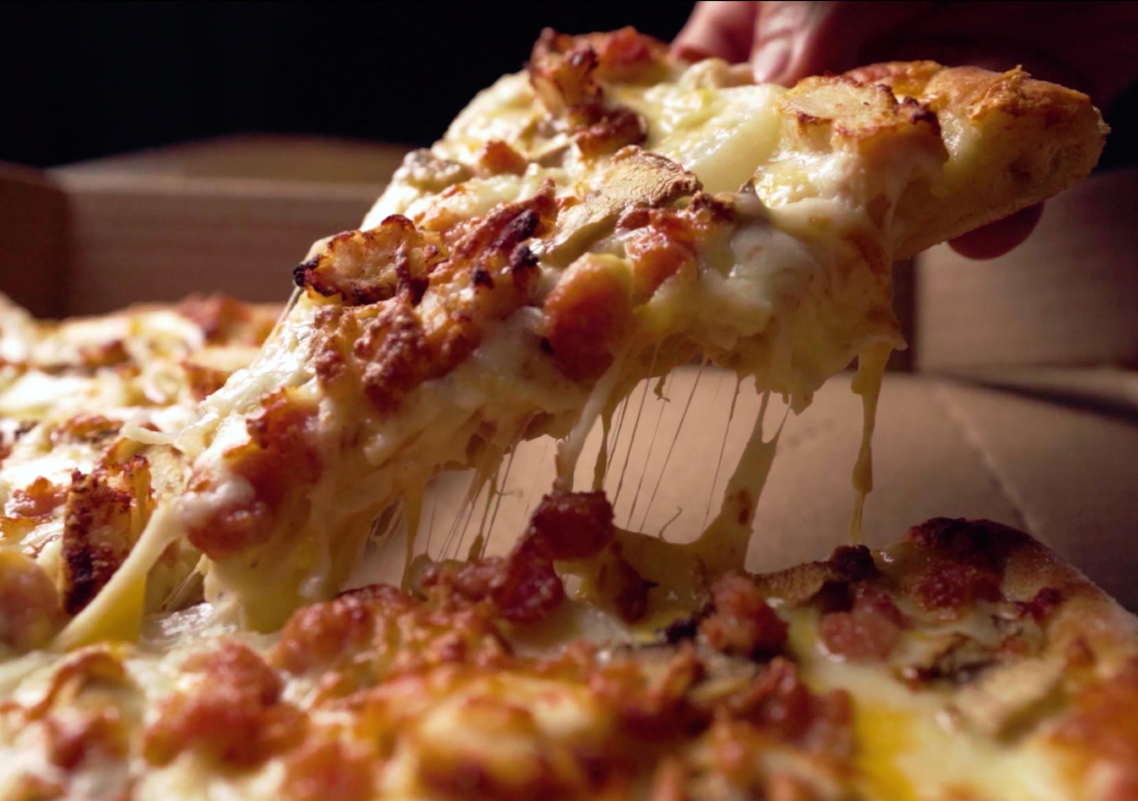 Person picking up a cheesy slice of Domino's pizza